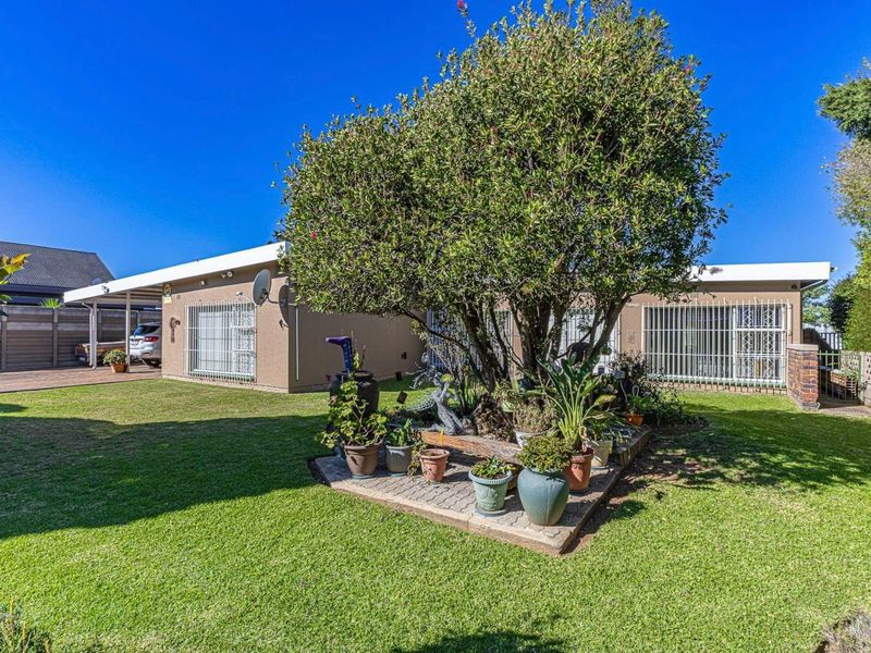 Rear exterior view of the house featuring a well-maintained lawn, a paved garden bed, security bars on windows, and an attached carport.