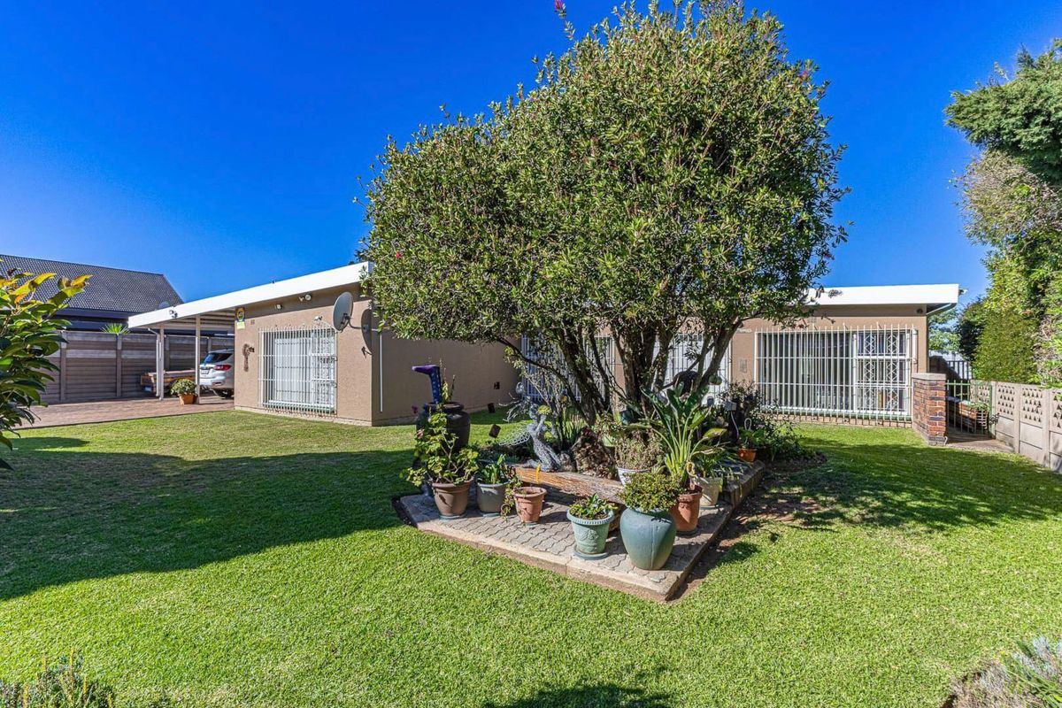 Rear exterior view of the house featuring a well-maintained lawn, a paved garden bed, security bars on windows, and an attached carport.