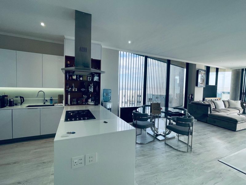 Modern open-plan apartment featuring a sleek kitchen with a central island, gas hob, and floor-to-ceiling windows offering ample natural light.