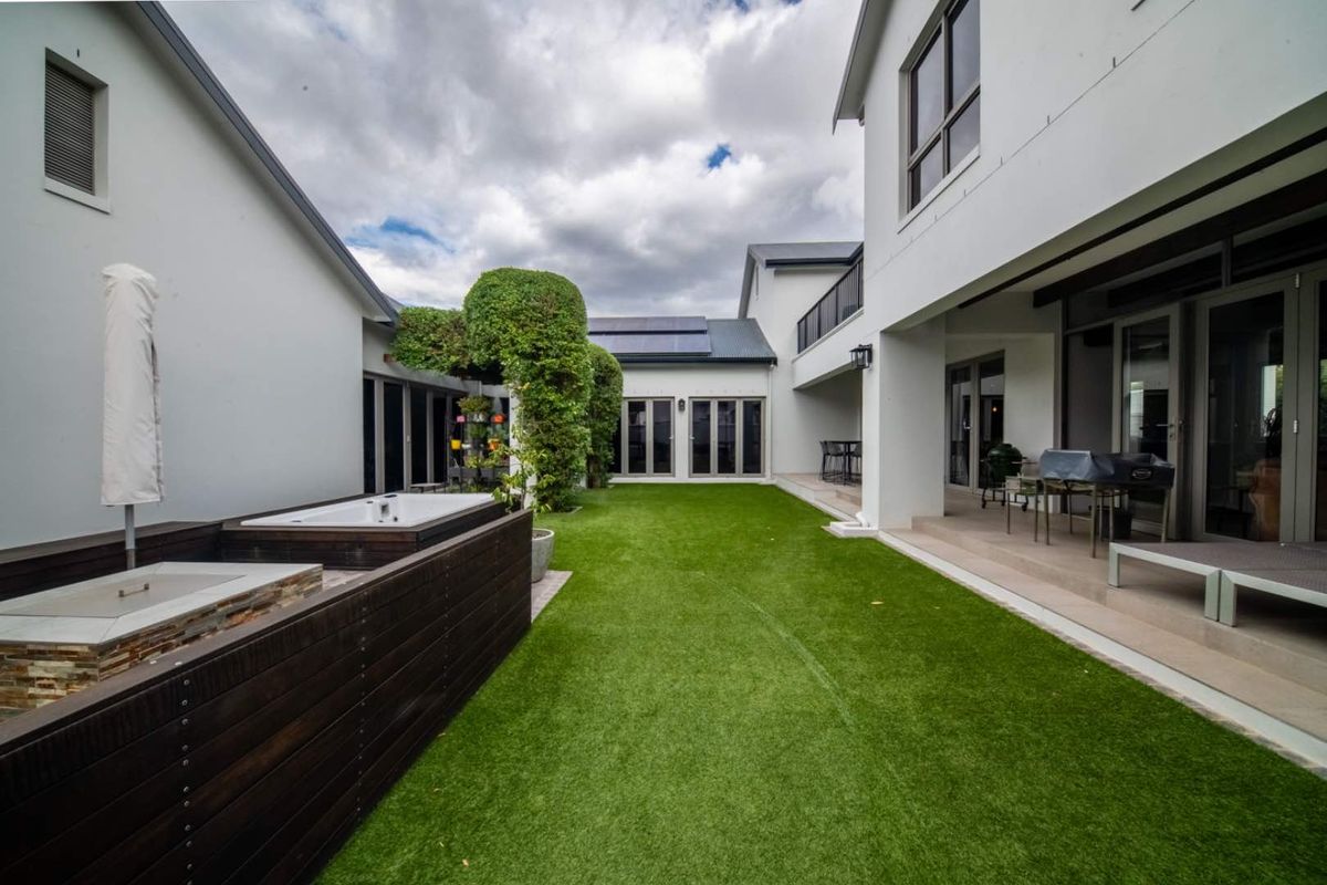 A well-maintained rear courtyard featuring artificial lawn, a built-in spa with timber decking, and a covered patio area accessible via sliding glass doors.