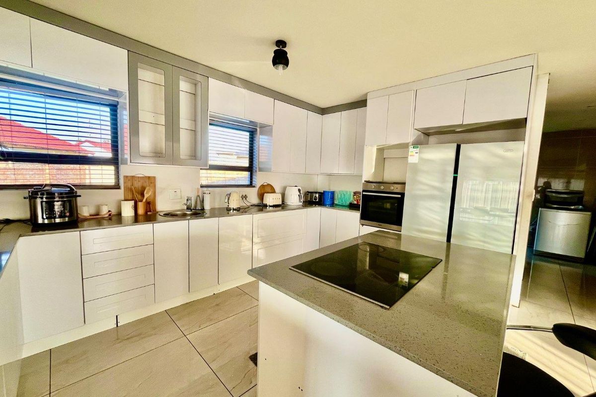 Modern kitchen featuring white high-gloss cabinetry, stone countertops, integrated oven, electric hob, and large format floor tiles.