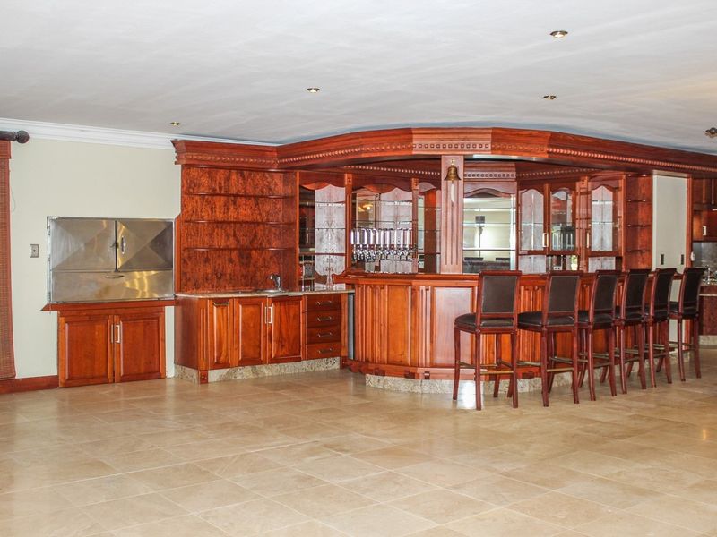A spacious entertainment area featuring a large, custom-built wooden bar with integrated cabinetry, sink, and a built-in stainless steel braai.