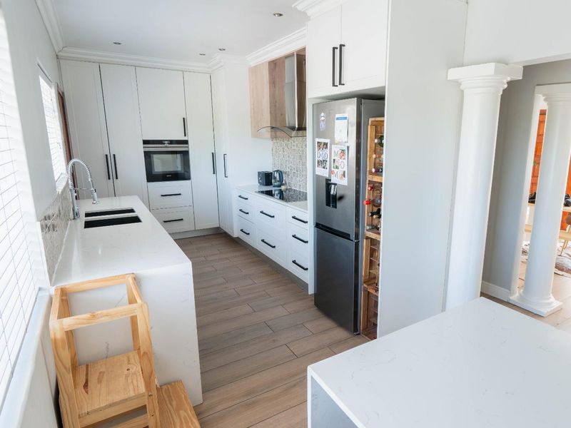 Modern kitchen featuring sleek white cabinetry, quartz countertops, integrated appliances, and a stylish tiled backsplash, complemented by wood-look flooring and decorative architectural columns.