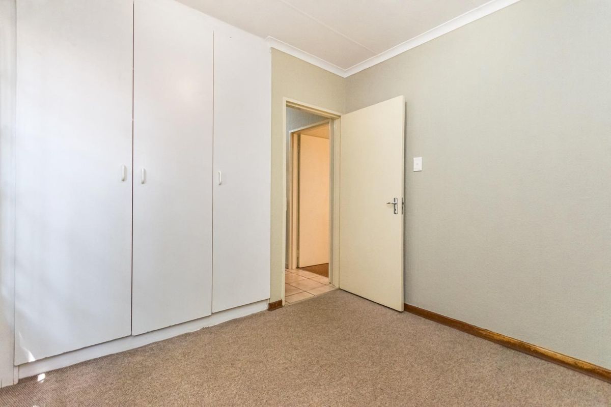 A clean, empty bedroom featuring neutral walls, carpeted flooring, and built-in cupboards, offering a versatile space ready for personalization.