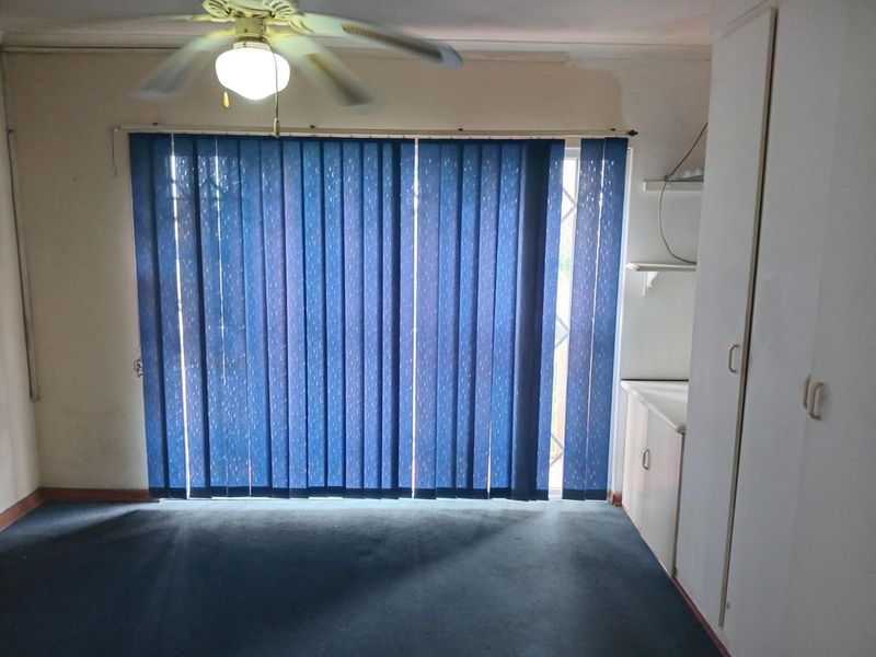 An empty living room featuring a ceiling fan, built-in storage cupboards, and a sliding door with vertical blinds leading to the exterior.