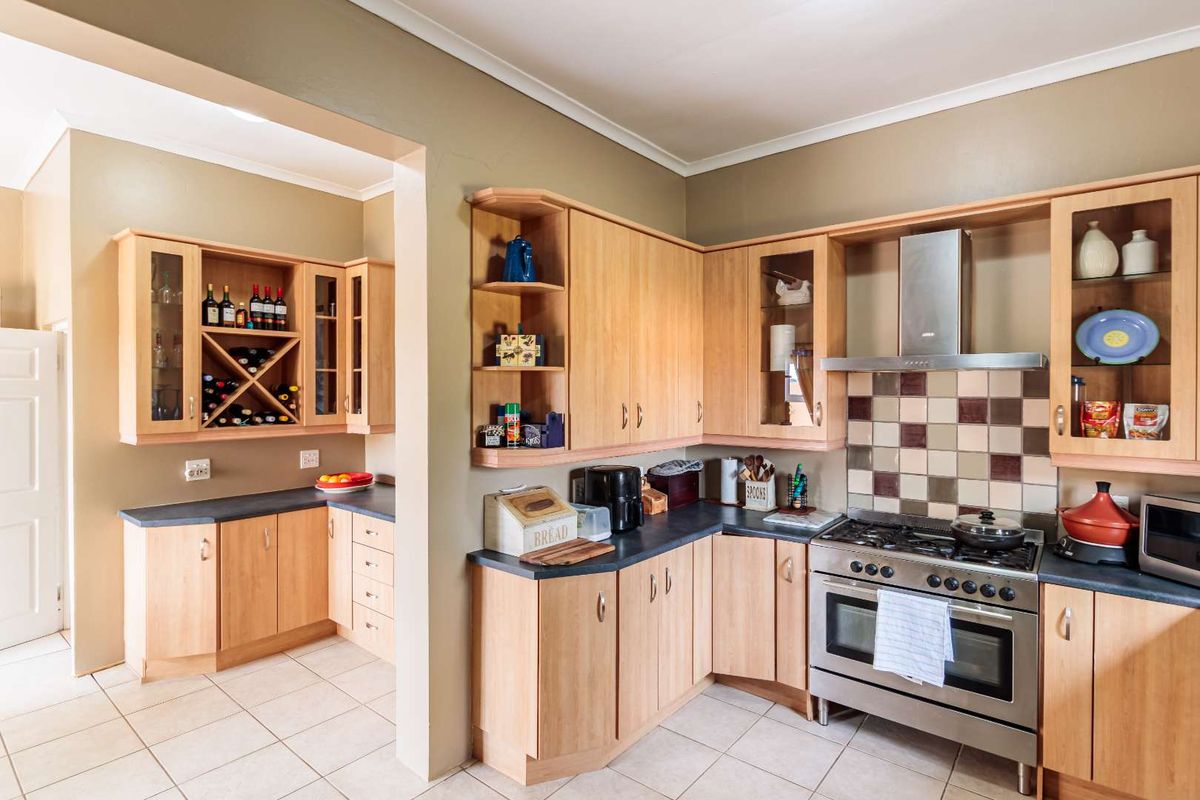 A functional kitchen featuring light wood cabinetry, a stainless steel gas stove with extractor fan, and tiled splashbacks, with an adjacent pantry or prep area.