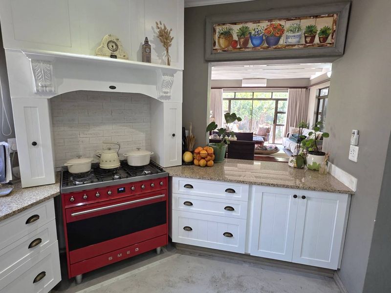 A well-appointed kitchen featuring a prominent red Smeg range cooker, granite countertops, and classic white cabinetry with a view into the adjacent living area.