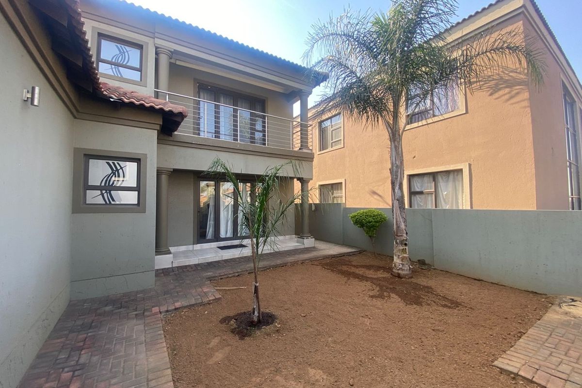 Rear view of the property featuring a paved patio area, a balcony with metal railings, and an enclosed garden space.