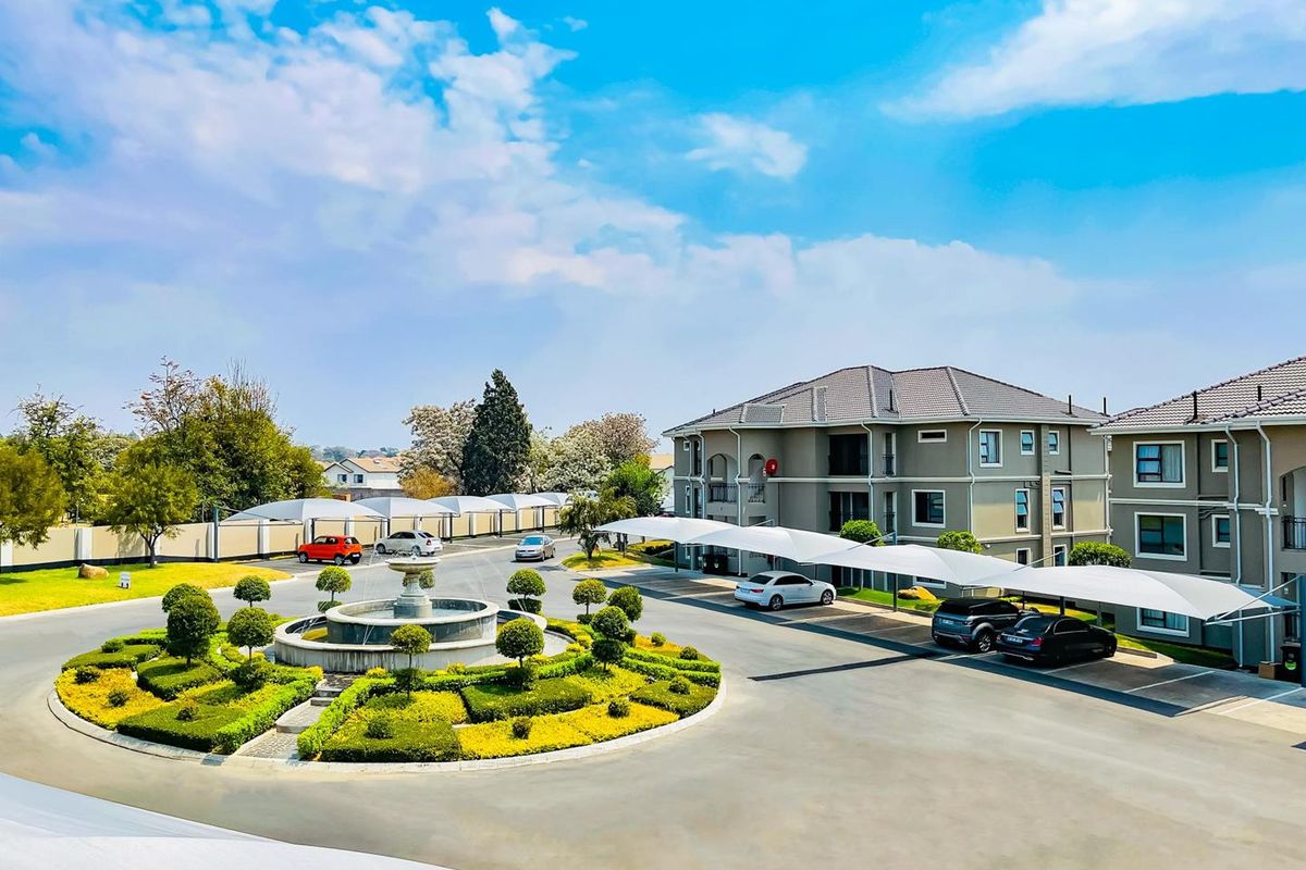 Aerial view of the apartment complex grounds featuring a central landscaped roundabout with a fountain, paved driveways, and covered parking bays.