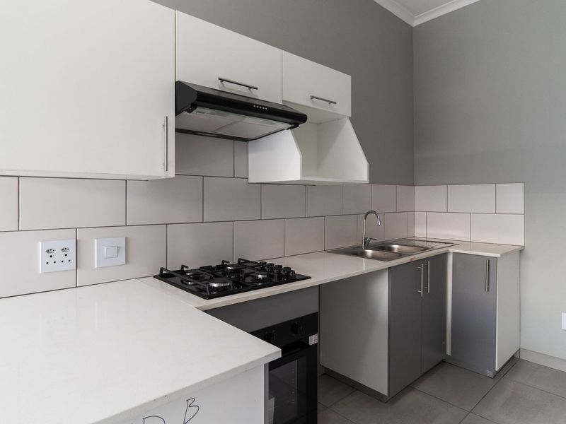 Modern kitchen featuring white cabinetry, stone countertops, a gas hob, built-in oven, extractor fan, and a stainless steel sink with a tiled backsplash.