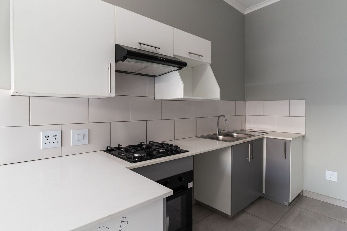 Modern kitchen featuring white cabinetry, stone countertops, a gas hob, built-in oven, extractor fan, and a stainless steel sink with a tiled backsplash.
