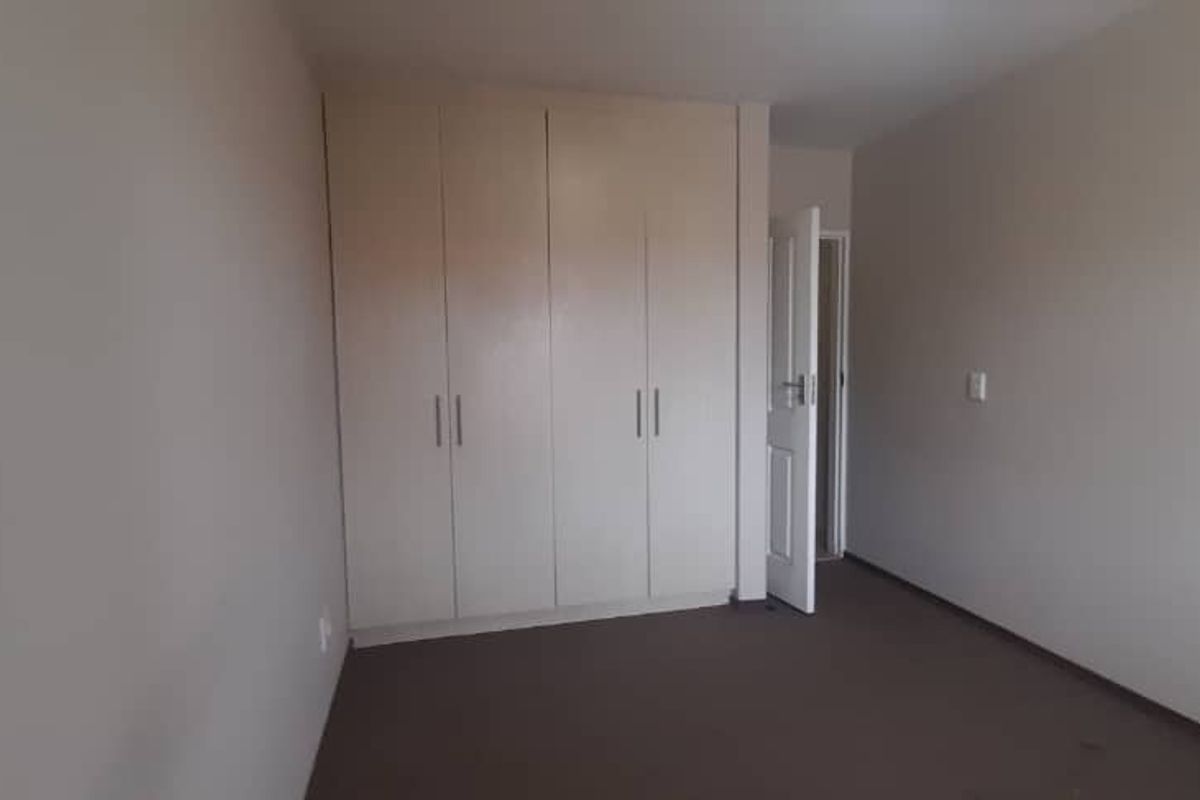 A bedroom featuring neutral wall tones, fitted built-in wardrobes, and carpeted flooring, offering a clean and functional living space.