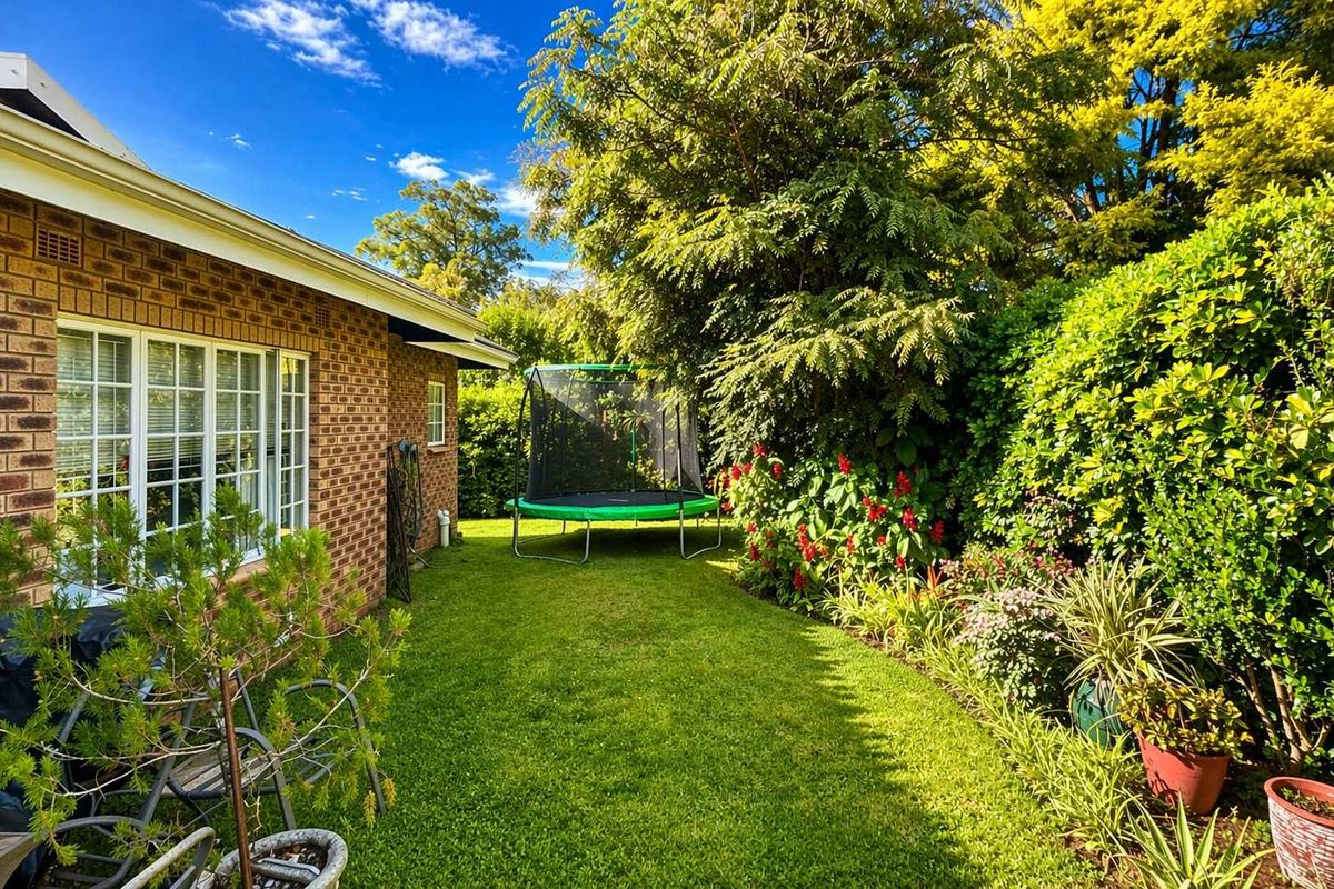 A well-maintained rear garden area featuring a brick exterior facade, lush green lawn, and established perimeter landscaping.