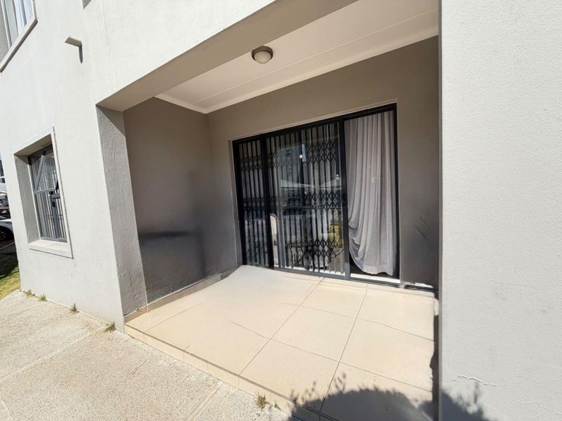 A covered patio area featuring tiled flooring, a sliding glass door with a security gate, and neutral wall finishes.