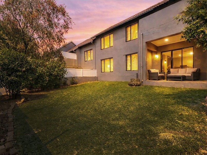 Rear view of the apartment building featuring a covered patio area, sliding glass doors, and a private lawn space at dusk.