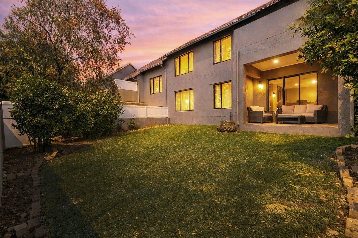 Rear view of the apartment building featuring a covered patio area, sliding glass doors, and a private lawn space at dusk.