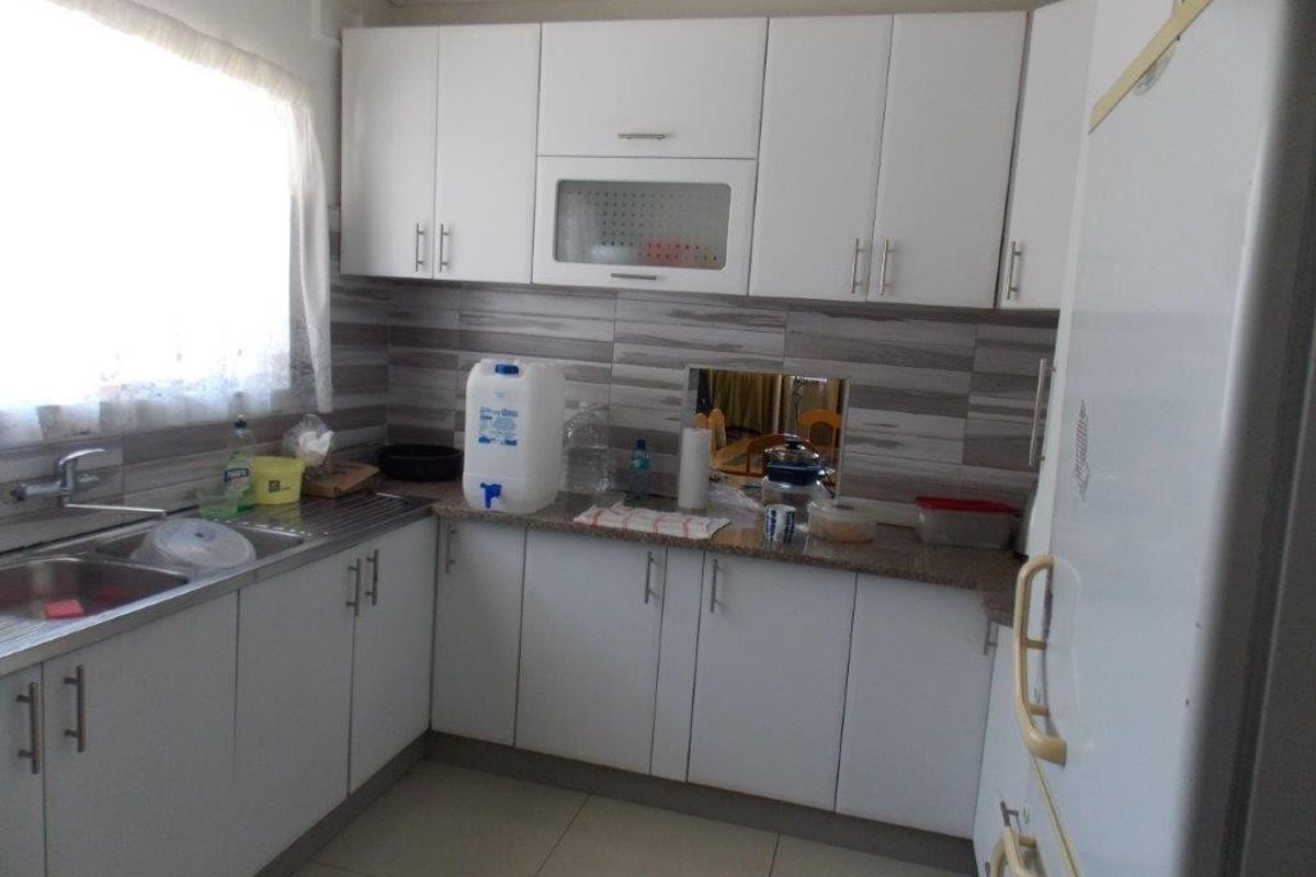 A functional kitchen featuring white cabinetry, laminate countertops, a stainless steel double sink, and a tiled backsplash.