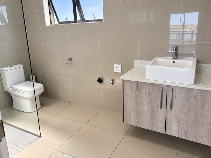 Modern bathroom featuring a wall-mounted vanity with a vessel sink, stone countertop, glass shower partition, and neutral tiled finishes.