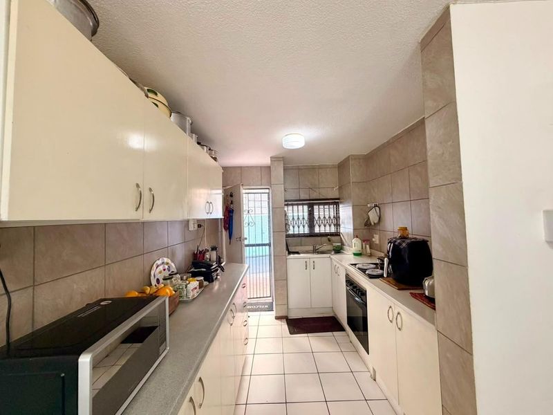 A functional galley-style kitchen featuring tiled flooring, ample built-in cabinetry, a built-in oven, and a tiled backsplash with direct access to an outdoor area.