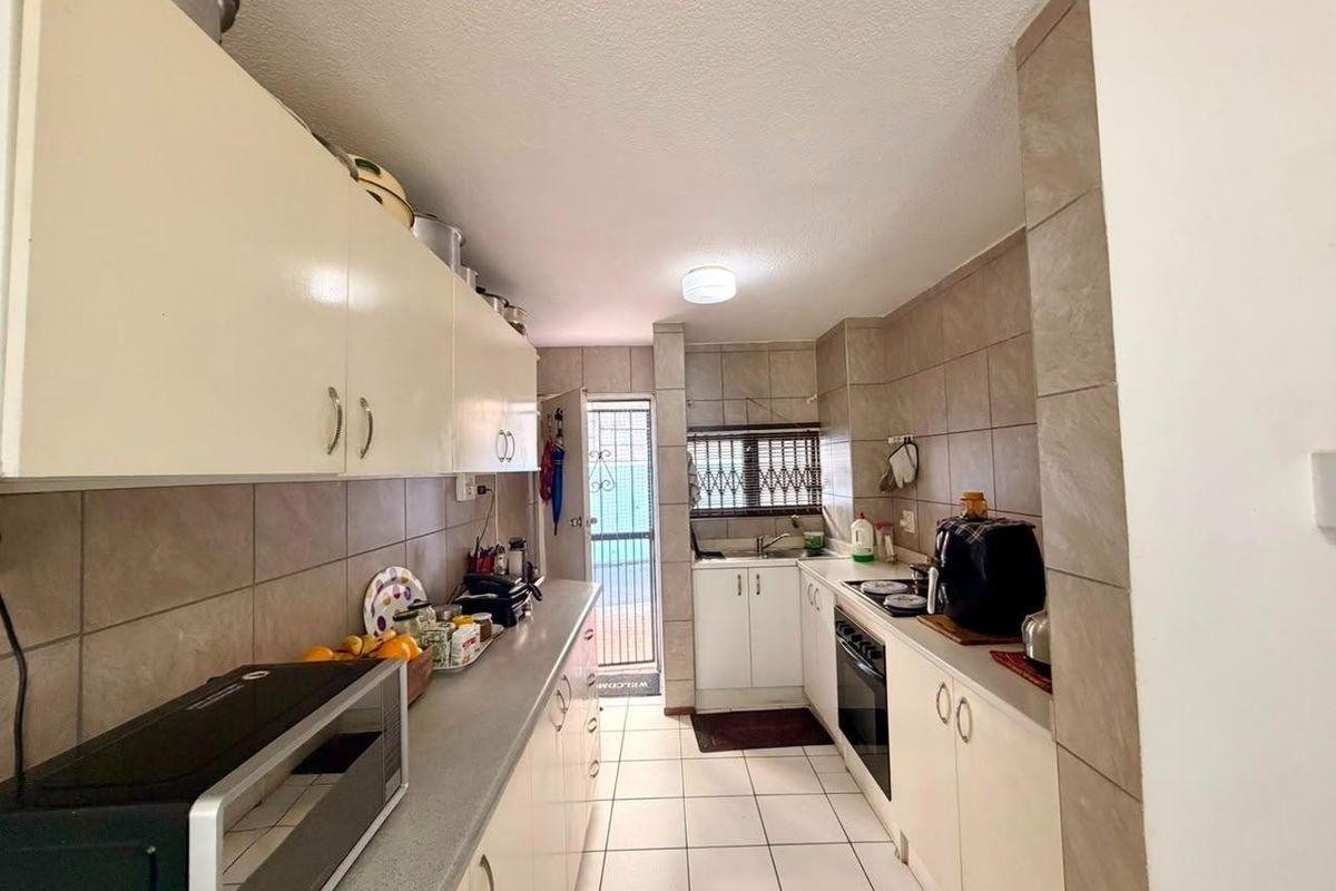 A functional galley-style kitchen featuring tiled flooring, ample built-in cabinetry, a built-in oven, and a tiled backsplash with direct access to an outdoor area.