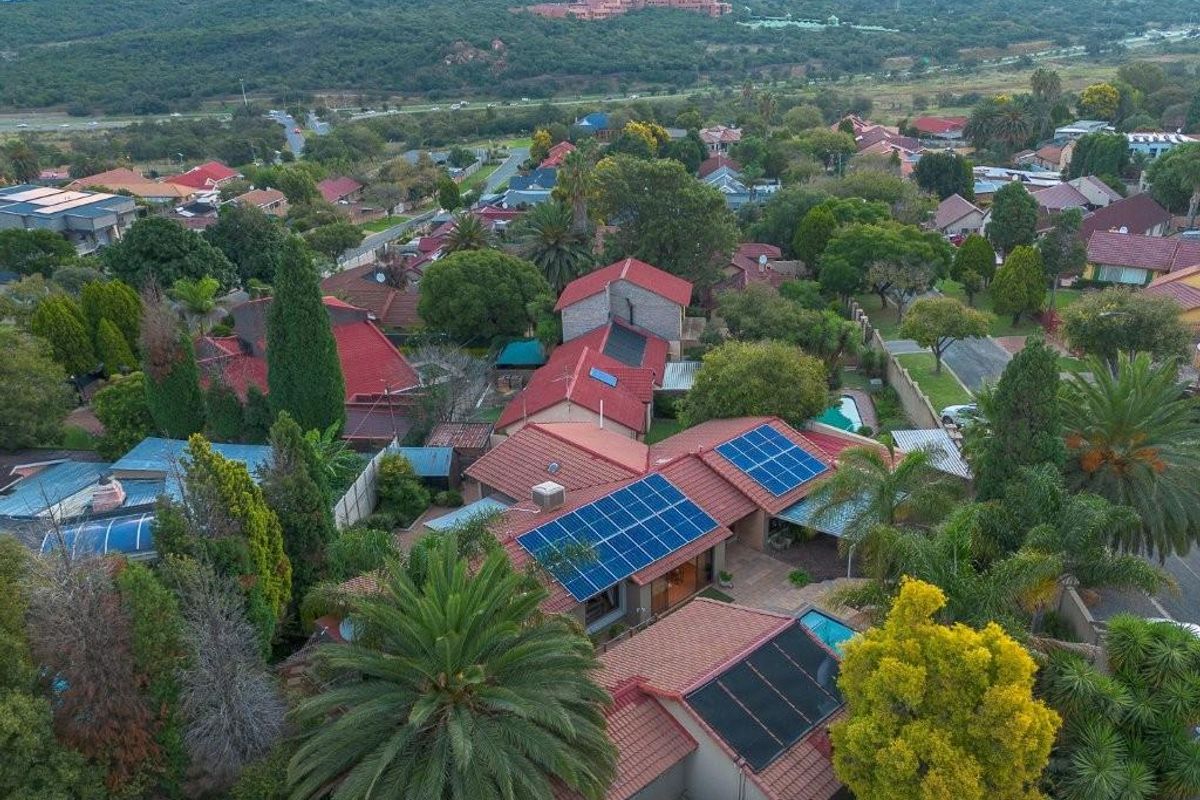 Aerial view of a residential property featuring a tiled roof with integrated solar panels and a swimming pool set within a landscaped garden.