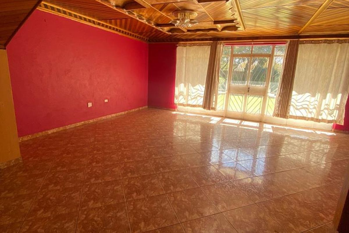Spacious living area featuring a distinctive timber-paneled ceiling, large glass sliding doors providing natural light, and tiled flooring throughout.