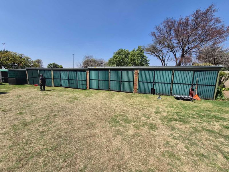 A view of the rear garden featuring a long row of corrugated metal fencing with brick support pillars.