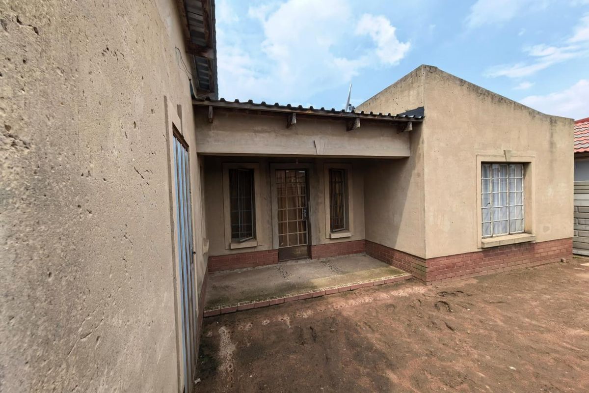 A rear exterior view of the house featuring a covered patio area with brick base and plaster walls.