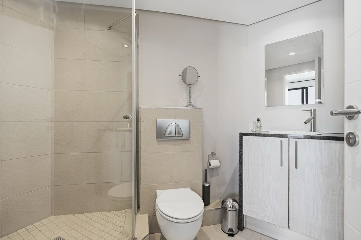 Modern bathroom featuring a walk-in shower with glass screen, wall-mounted toilet with concealed cistern, and a vanity unit with stone countertop.