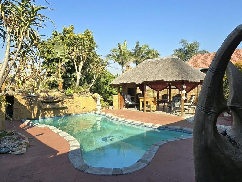 Outdoor pool area featuring a swimming pool, stone-clad water feature, and a thatched lapa, providing a functional space for outdoor entertainment.
