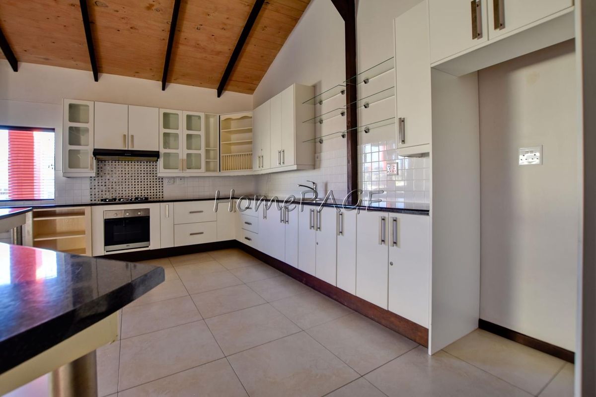 Spacious kitchen featuring white cabinetry, dark countertops, tiled flooring, and a vaulted timber ceiling with exposed beams.