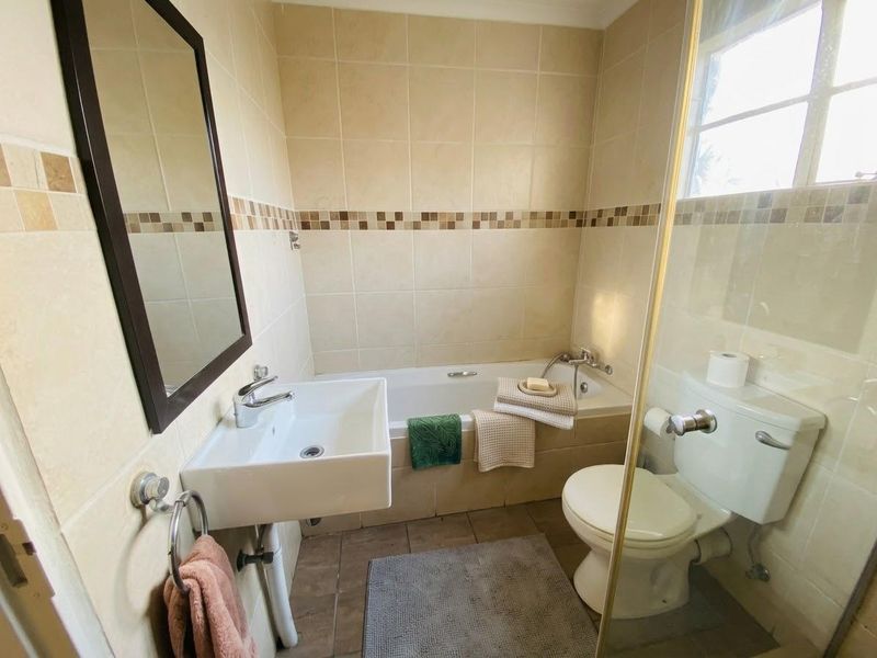 A functional bathroom featuring a wall-mounted basin, built-in bathtub, and toilet with neutral wall tiling and a shower screen.