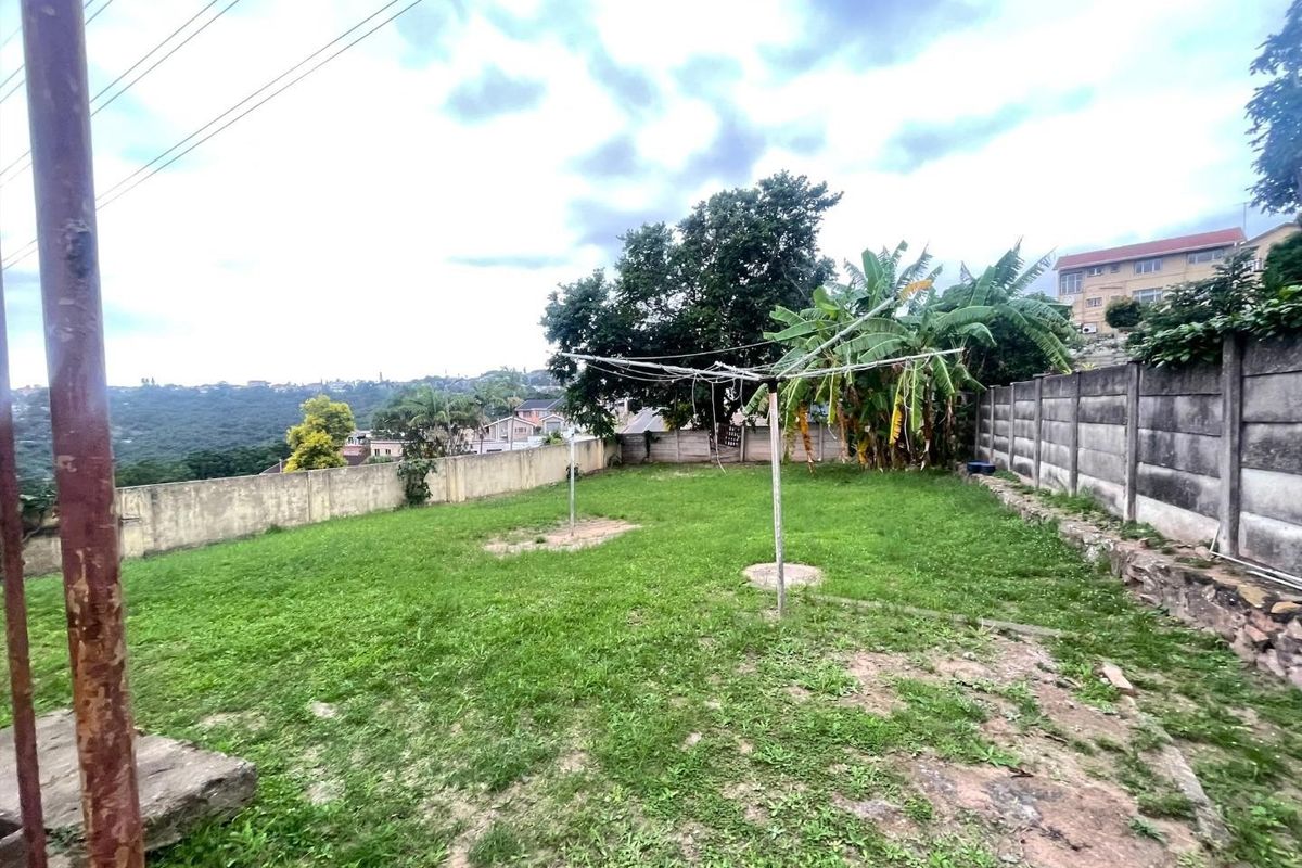 A spacious rear garden area featuring a precast concrete boundary wall, rotary clothesline, and established greenery with views of the surrounding neighborhood.