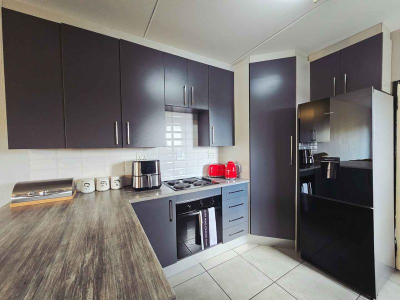 Modern kitchen featuring dark grey cabinetry, wood-look laminate countertops, tiled backsplash, and integrated oven and hob.