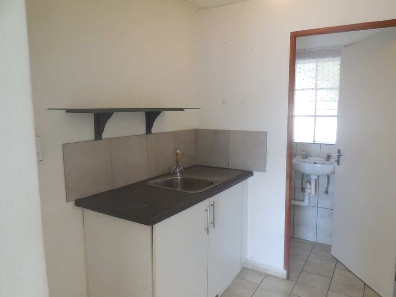 A compact kitchenette featuring a stainless steel sink, laminate countertop, base cabinetry, and tiled splashback, with an adjacent small bathroom visible.