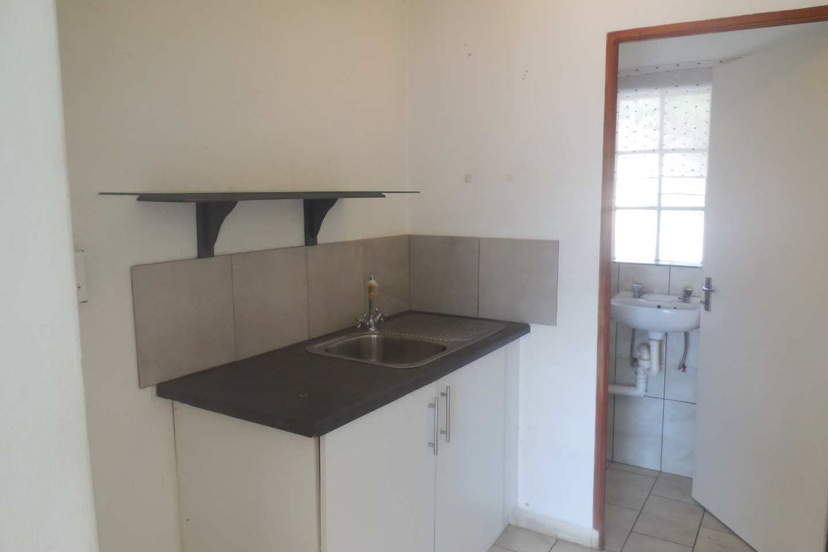 A compact kitchenette featuring a stainless steel sink, laminate countertop, base cabinetry, and tiled splashback, with an adjacent small bathroom visible.