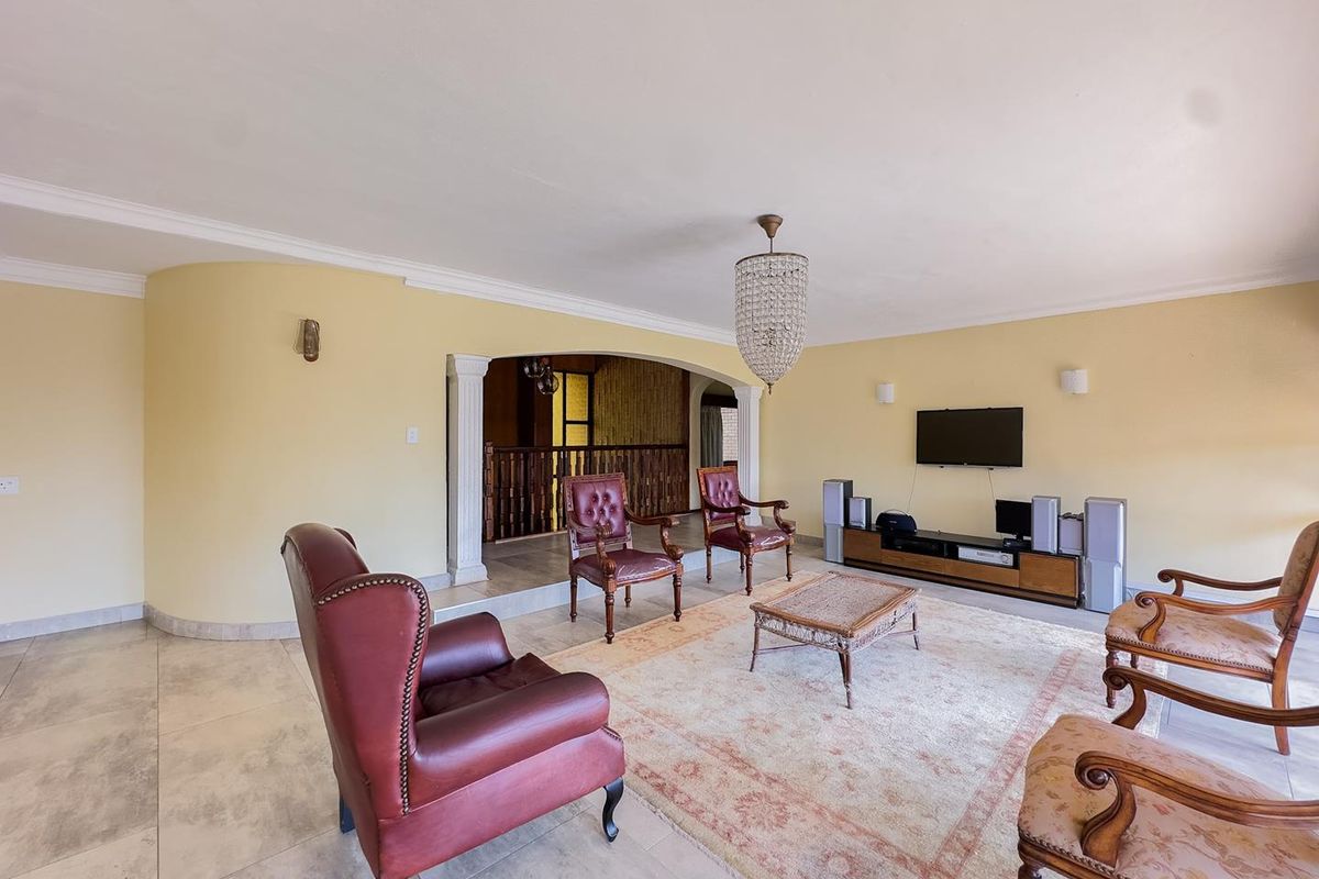 Spacious living room featuring tiled flooring, decorative crown molding, a central crystal chandelier, and an arched entryway leading to an adjacent area.