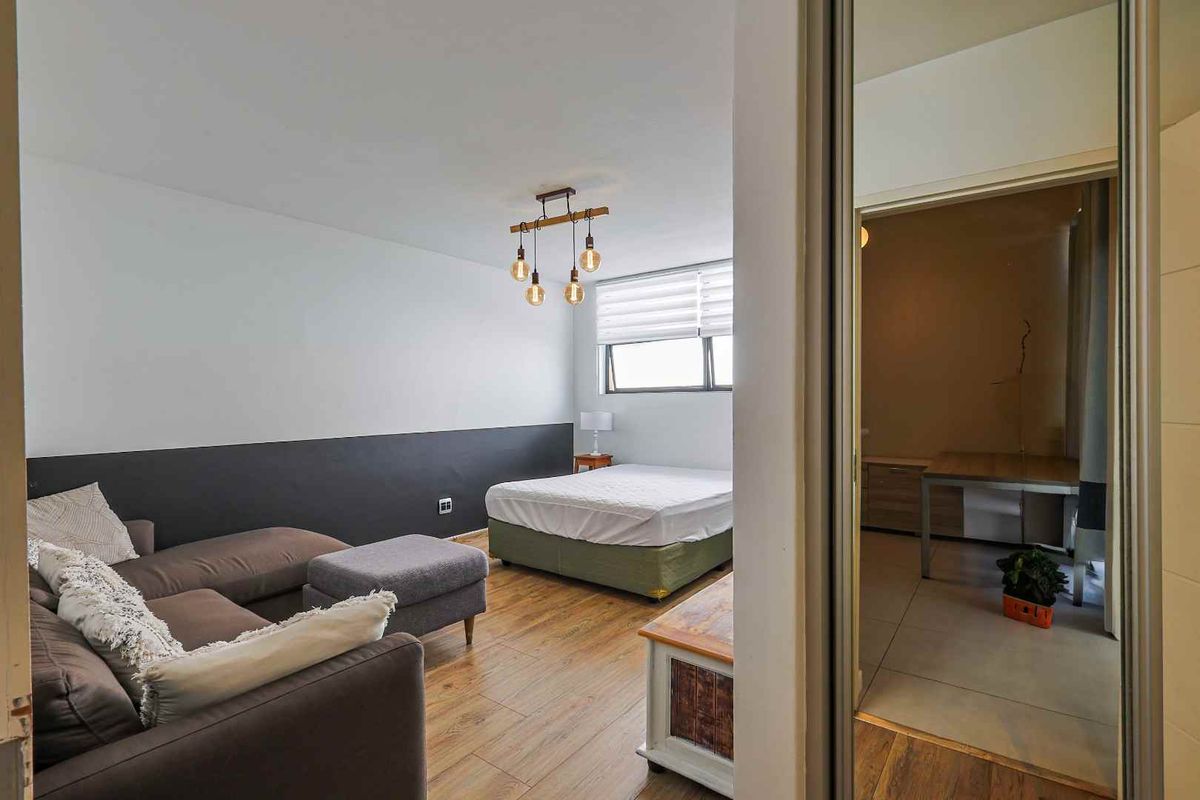 A view into a bedroom featuring wood-look flooring, a modern pendant light fixture, and an adjacent room visible through the doorway.