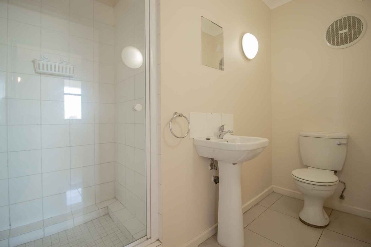 A functional bathroom featuring a shower enclosure, pedestal basin, and toilet with neutral wall finishes and tiled flooring.