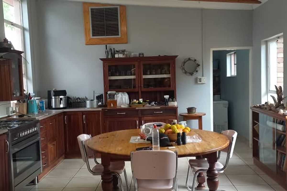 A functional kitchen featuring wooden cabinetry, a gas stove with extractor fan, and tiled flooring, with an adjacent scullery area.