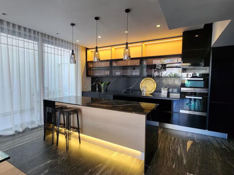 Modern, high-end kitchen featuring sleek black cabinetry, a stone-topped island with integrated lighting, and premium built-in appliances.