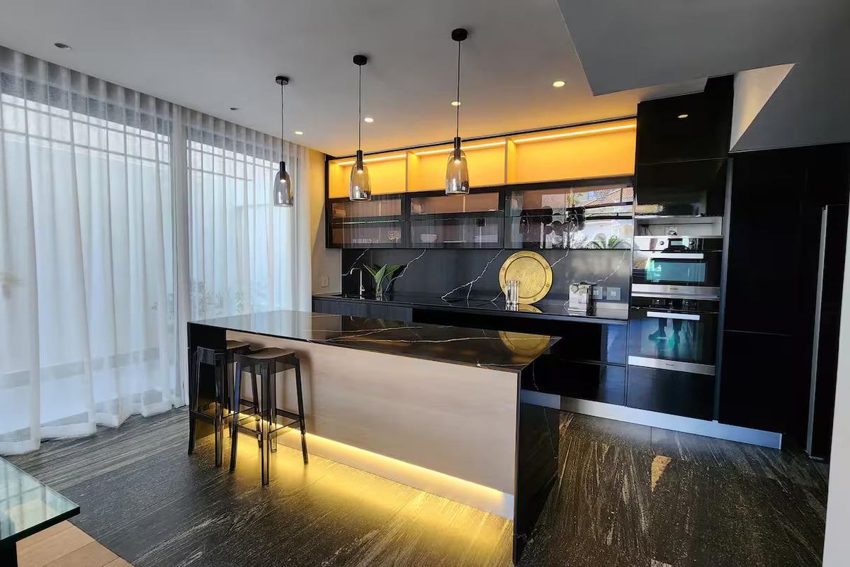 Modern, high-end kitchen featuring sleek black cabinetry, a stone-topped island with integrated lighting, and premium built-in appliances.