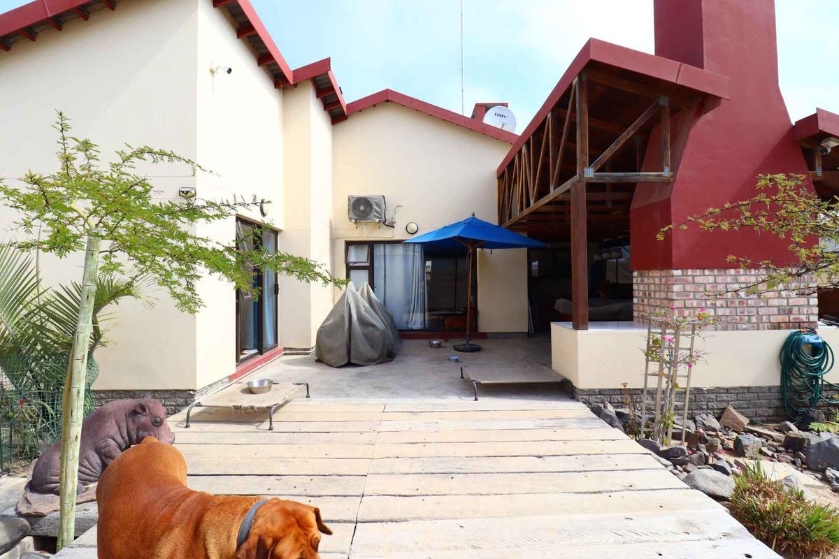 Rear exterior view featuring a covered patio area with a brick fireplace, timber decking, and sliding glass door access to the main house.