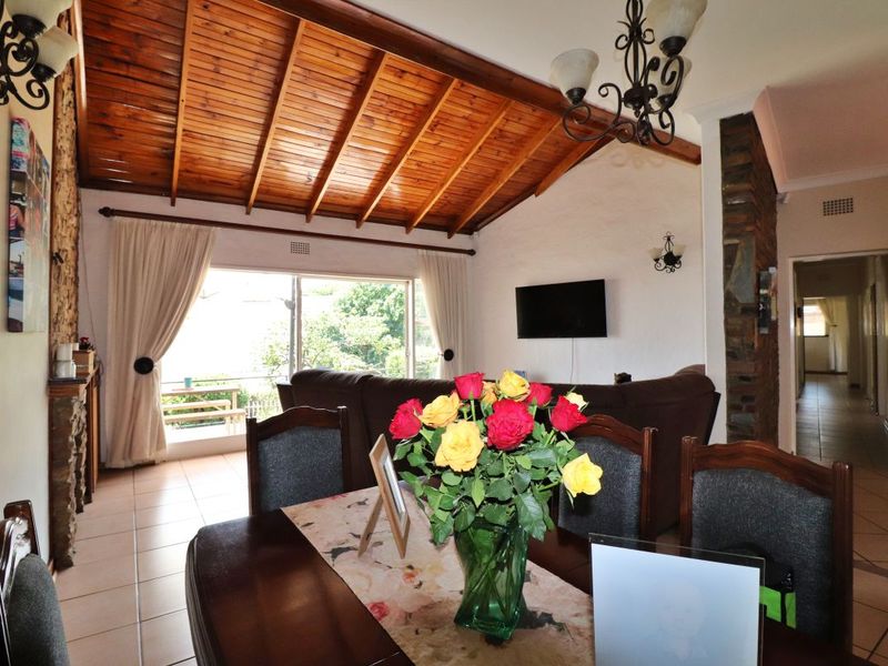 Spacious open-plan living and dining area featuring a high exposed timber rafter ceiling, stone feature wall, and large sliding doors leading to the outdoors.