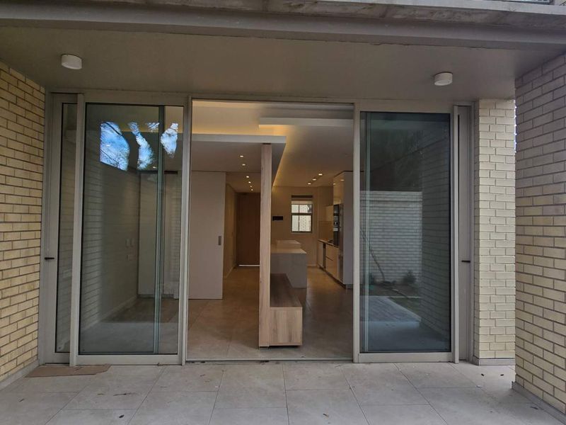 A modern covered patio featuring large sliding glass doors that provide seamless access to the open-plan interior living and kitchen area.