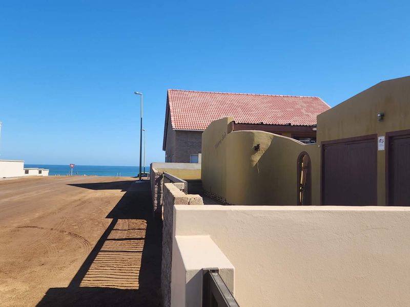 A street-level view showing the property exterior, boundary walls, and garage access, with a clear view of the nearby coastline.