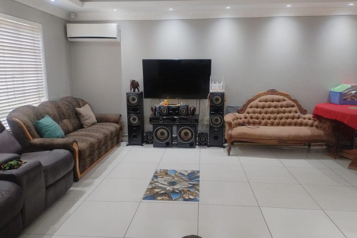 Spacious living room featuring large format floor tiles, recessed ceiling lighting with decorative molding, and a wall-mounted air conditioning unit.