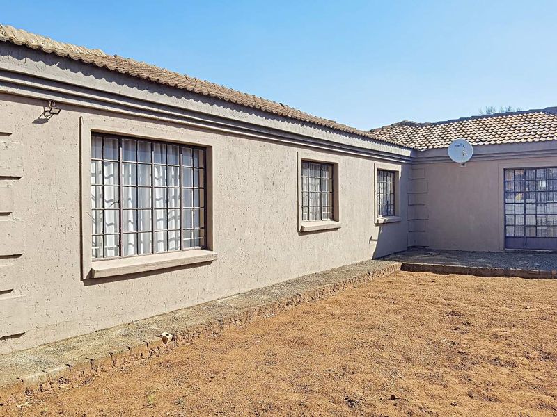 Rear view of a single-story house featuring a tiled roof, security bars on windows, and an unlandscaped yard area.
