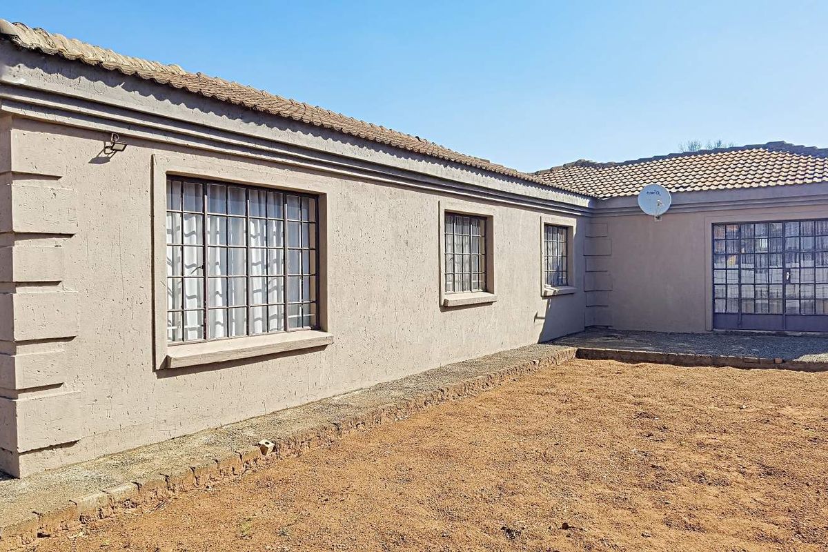 Rear view of a single-story house featuring a tiled roof, security bars on windows, and an unlandscaped yard area.