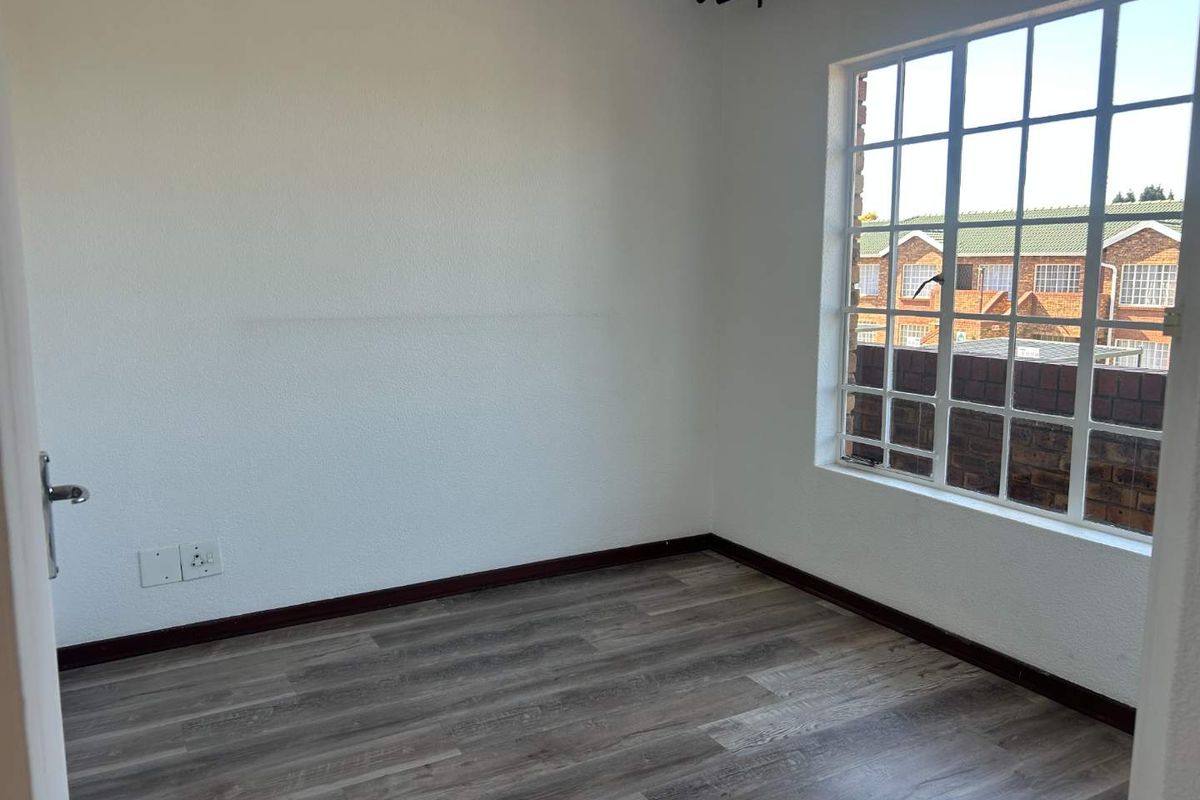An empty bedroom featuring modern laminate flooring, a large grid-pattern window, and neutral white walls, providing a clean and versatile living space.
